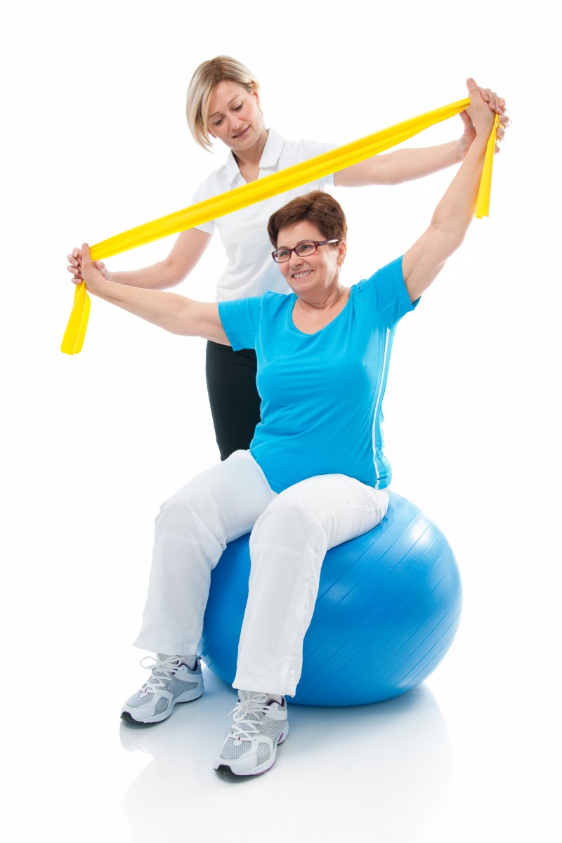photo-une-consultation-physiotherapie-avec-une-femme-assise-sur-gros-ballon-etirant-les-bras-avec-une-bande-elastique